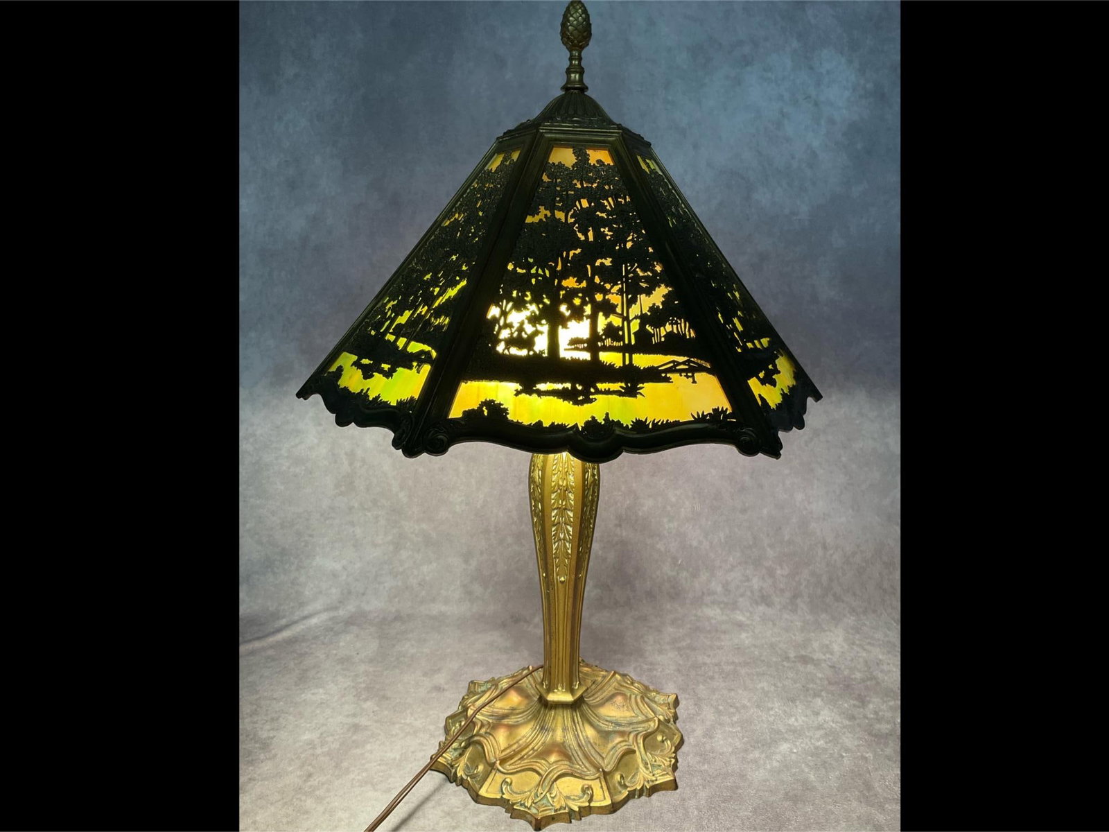 Early 20th C. Slag Glass Lamp: Green slag glass shade with scene of a man on horseback riding through the woods towards a church. All six panels reflect this scene. One glass panel is broken, some of the pieces are included. Anothe