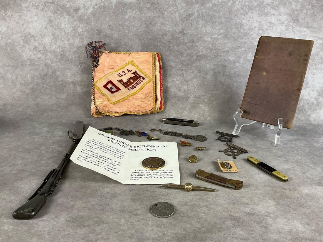 Gentleman's Military Lot: Fabric Engineer book, three knives, rifle letter opener, WWII Marine Corps expert rifleman badge, bicentennial coin, enameled flag pins, military coins and buttons. First Geography for Natives book wi