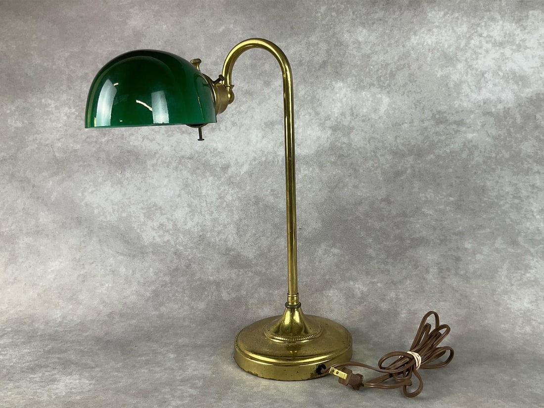 Brass Bankers Lamp: With green shade. Powers on. Some verdigris on base, but otherwise fair to good condition. Measures 5.5 inches wide at base x 16.5 inches tall.