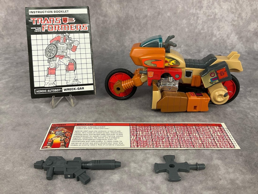 1986 Wreck-Gar Transformer: Made by Hasbro in Japan. Includes instruction booklet, tech spec card, and weapons. Missing decoder. Good condition but does have minor wear to decals. Transformer measures 6.5 inches long x 2.5 x 3.5