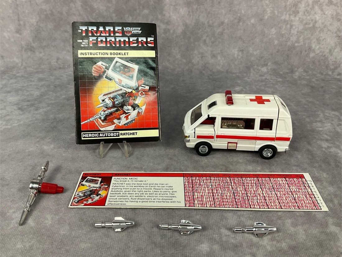1984 Ratchet Transformer: Made by Hasbro in Japan. Includes instruction booklet, tech spec card, and weapons. Missing decoder. Play wear, chipped paint in places, and wear to decals. Transformer measures 3.5 inches long x 1.75