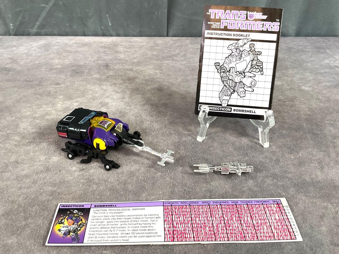 1984 Bombshell Transformer: Made by Hasbro in Japan. Includes instruction booklet, tech spec card, and weapons. Missing decoders. Good condition but has minor wear to decals. The transformer measures 4.5 inches long x 2 x 1.5 in