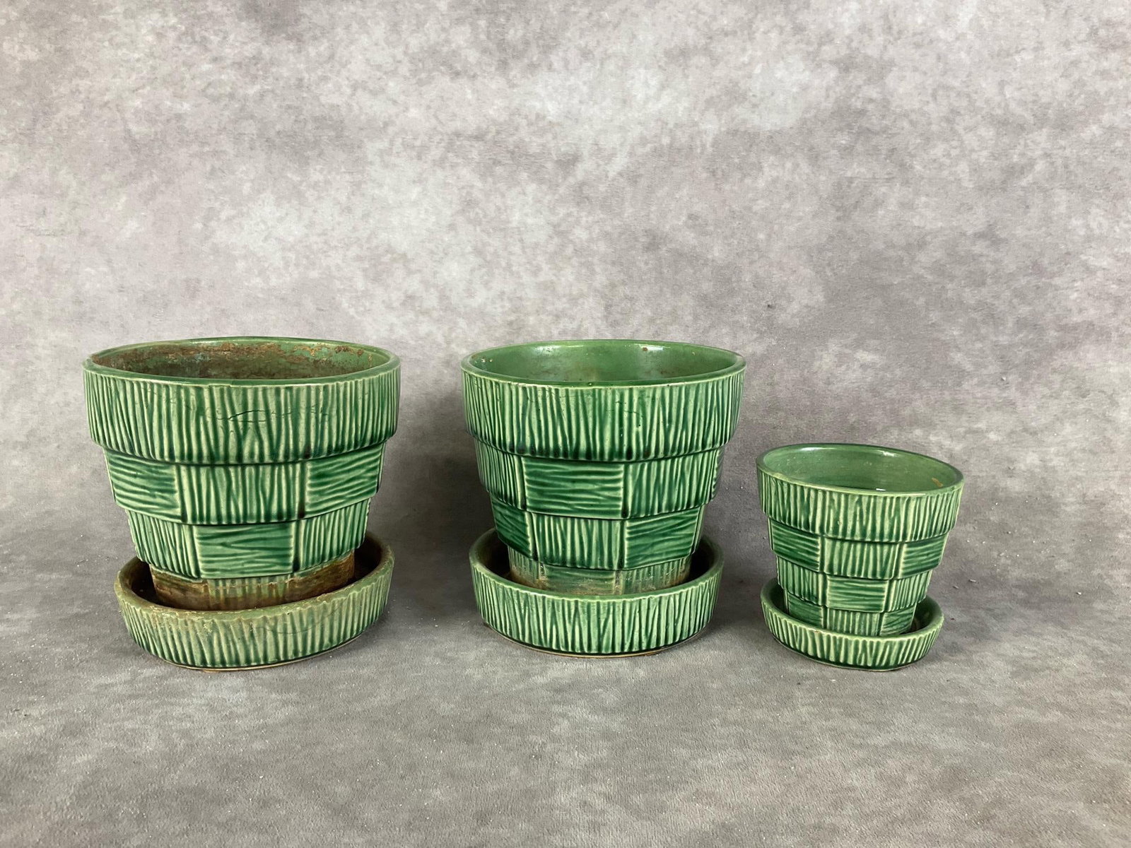 Mid-Century McCoy Basketweave Planter: 1953 set of three, with pots and saucers. Marked on bottom. Sizes are 6.5, and 3.5 inches in diameter. Crazing and water marks present, Largest planter measures 6 inches tall.