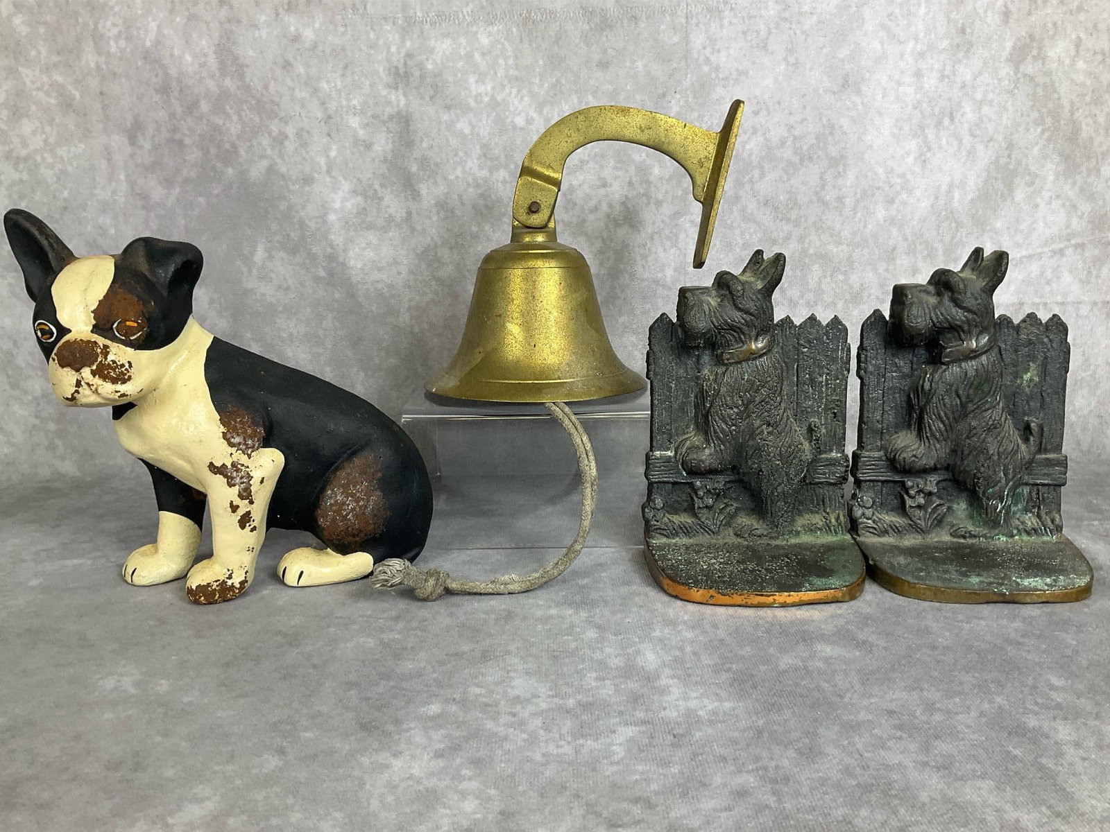 Cast Iron Dogs & Brass Bell: Scottish terrier cast brass bookends, contemporary cast iron Boston terrier doorstop, and a brass dinner bell. All have patina and rust. Doorstop measures 7 inches wide x 3 x 7.25 inches tall.