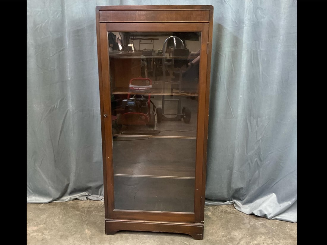 Art Deco Bookcase: 1920s locking glass front bookcase with original key and adjustable shelves. Scratches to top and to feet. Measures 24 inches long x 12.25 x 53.25 inches tall.