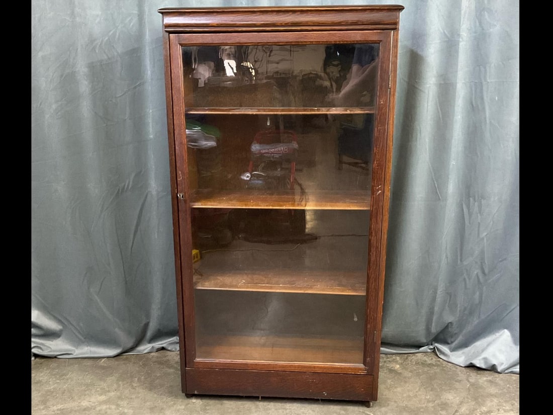 Art Deco Bookcase: 1920s locking glass front bookcase on casters with original key and adjustable shelves. Wear to shelves and a few scratches on cabinet. Measures 29 inches long x 13 x 53 inches tall.