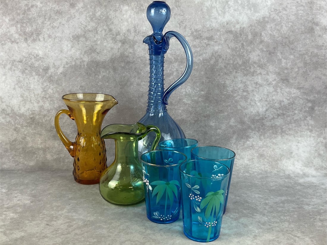 Colorful MCM Glass: One hand blown blue decanter, one amber teardrop hobnail pitcher, a hand blown green glass pitcher, and four teal hand painted glasses. All are in good condition. The blue decanter measures 5 inches w