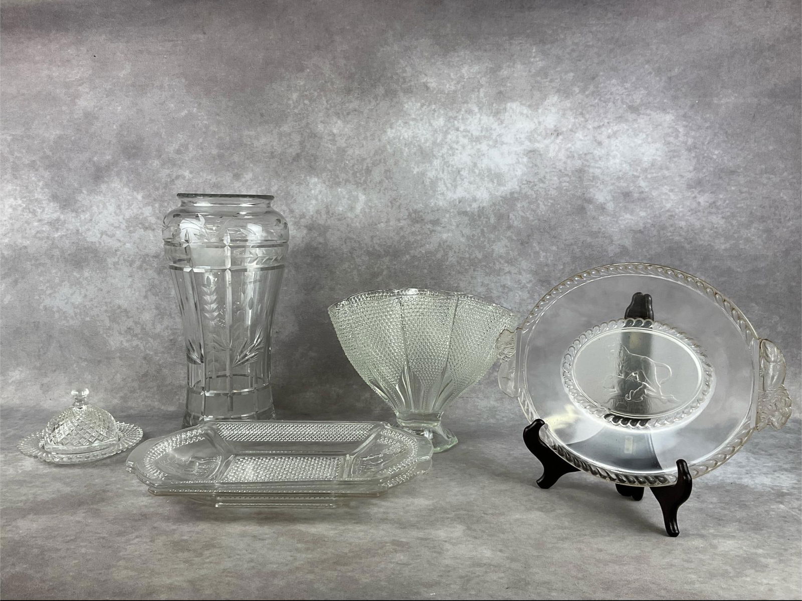McKee & Brothers Clear Glass: Two platters made by McKee and Bros., one domed butter dish, a large etched vase, a L.E. Smith hobnail fan vase, and a Gillinder and Sons dying lioness bread plate (circa 1877). All items are in good