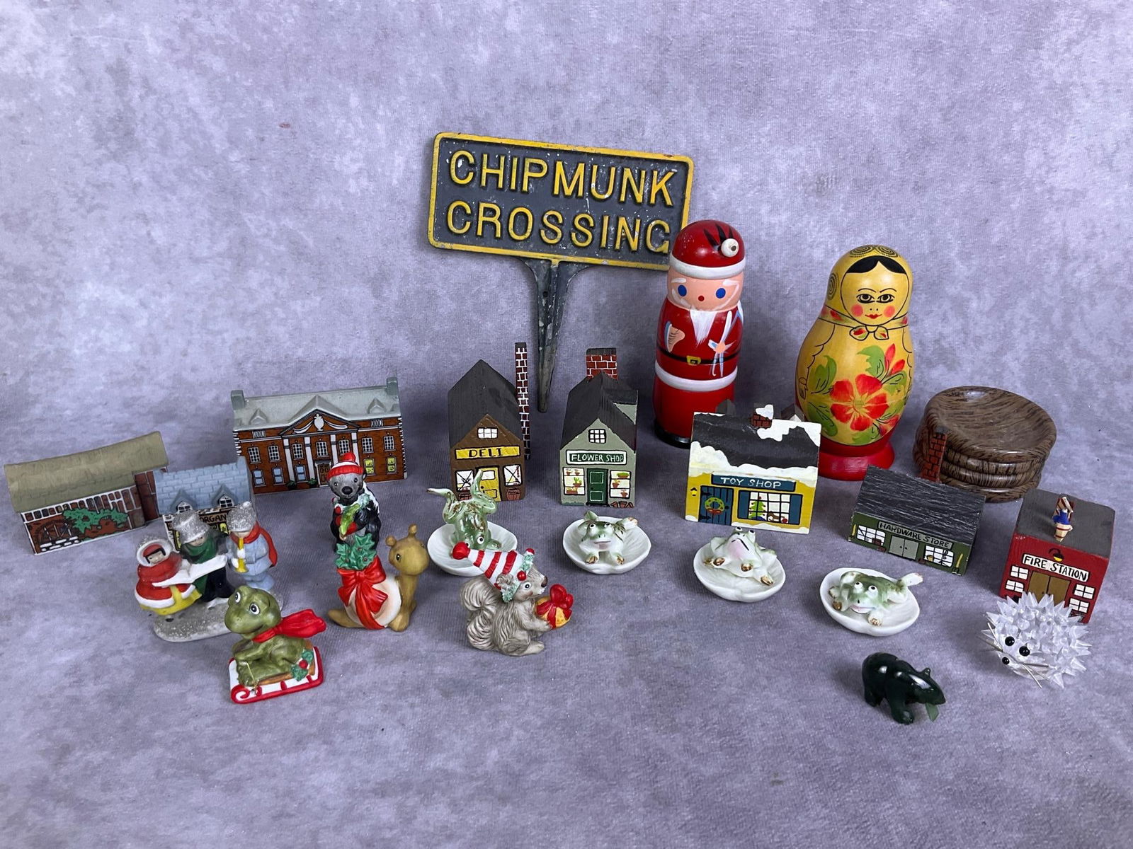 Holiday Trinkets & More: 26 pieces including miniature holiday ceramics, wooden buildings, frogs, nesting dolls and more. All appear in good condition. Chipmunk sign measures 6 inches wide x 6 inches tall.