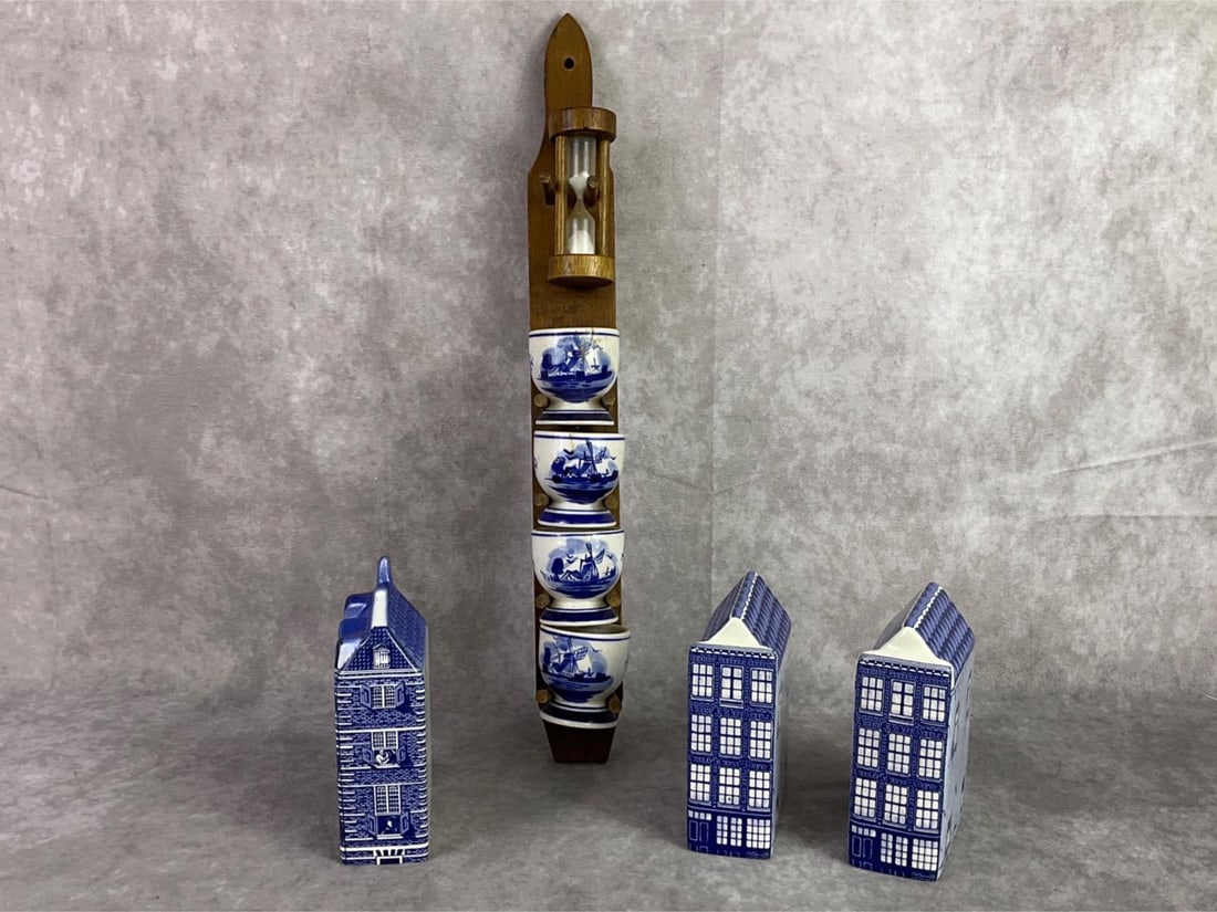 Anne Frankhuis Delft Items: Set of three Anne Frankhuis Delft houses and Delftware egg cups with holder and hourglass timer. All in good condition. Egg holder stand measures 1.5 inches wide x 15.5 inches tall.