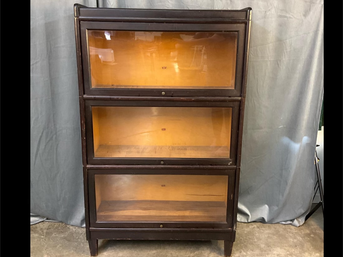 Weis Barrister Bookcase: Early 1900s three shelf barrister bookcase made by Weis in Michigan. Dark wood veneer with glass front doors that fold up and slide back. Each section has maker sticker on back panel. Veneer is peelin
