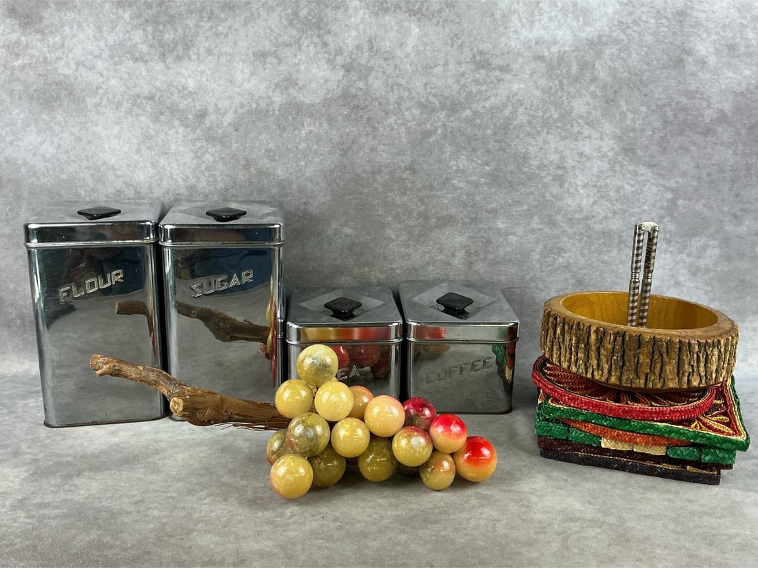Mid Century Kitchen Decor: Mixed lot of 1960s alabaster grape cluster, chrome Masterware canister set, nutcracker dish and a group of woven raffia trivets. All in fair to good condition. Flour canister measures 5 inches wide x