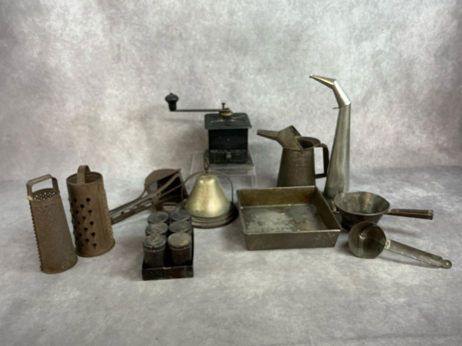 Primitive Metal Kitchen Collectibles: Twelve late 1800s to early 1900s kitchen items. Included are a coffee mill by Universal, Savory liquid tin pitcher, two bells, two round graters, ice cream scoop, potato ricer, and more. Rust present