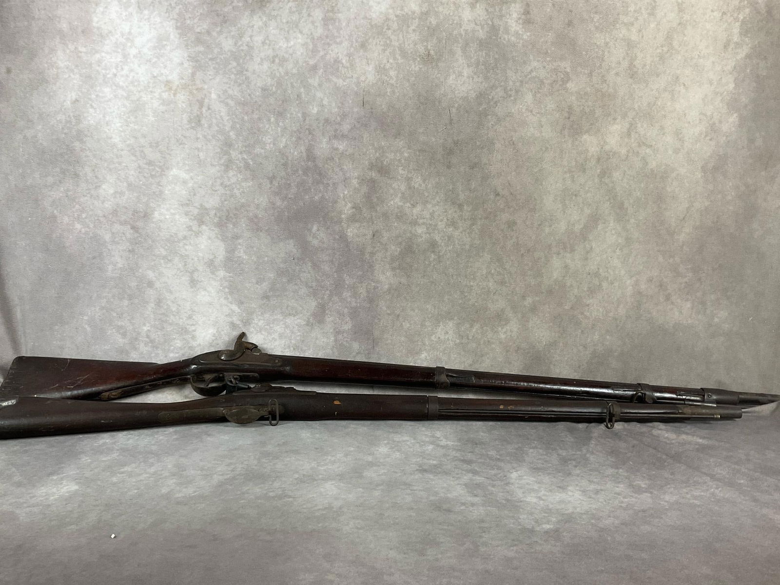 1884 U.S. Springfield Armory Trapdoor Rifle & Antique Blackpowder Rifle: One 1884 Springfield Armory trapdoor black powder rifle, and one unmarked black powder rifle. Both in poor condition with heavy rust, scratches and signs of age. Likely a historical decorative piece.
