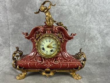 Early 1900s burgundy ceramic clock with glass face. Clock sits on brass sand. Cherub on the top has