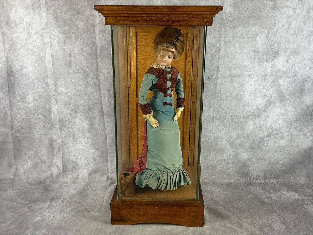 Late 1800s-early 1900s porcelain doll with mink hat and muff. Incased in a glass and oak case. The: Late 1800s-early 1900s porcelain doll with mink hat and muff. Incased in a glass and oak case. The dolls dress has fading, stains and is frayed. Case is handmade and solid. Case measures 11 inches wid