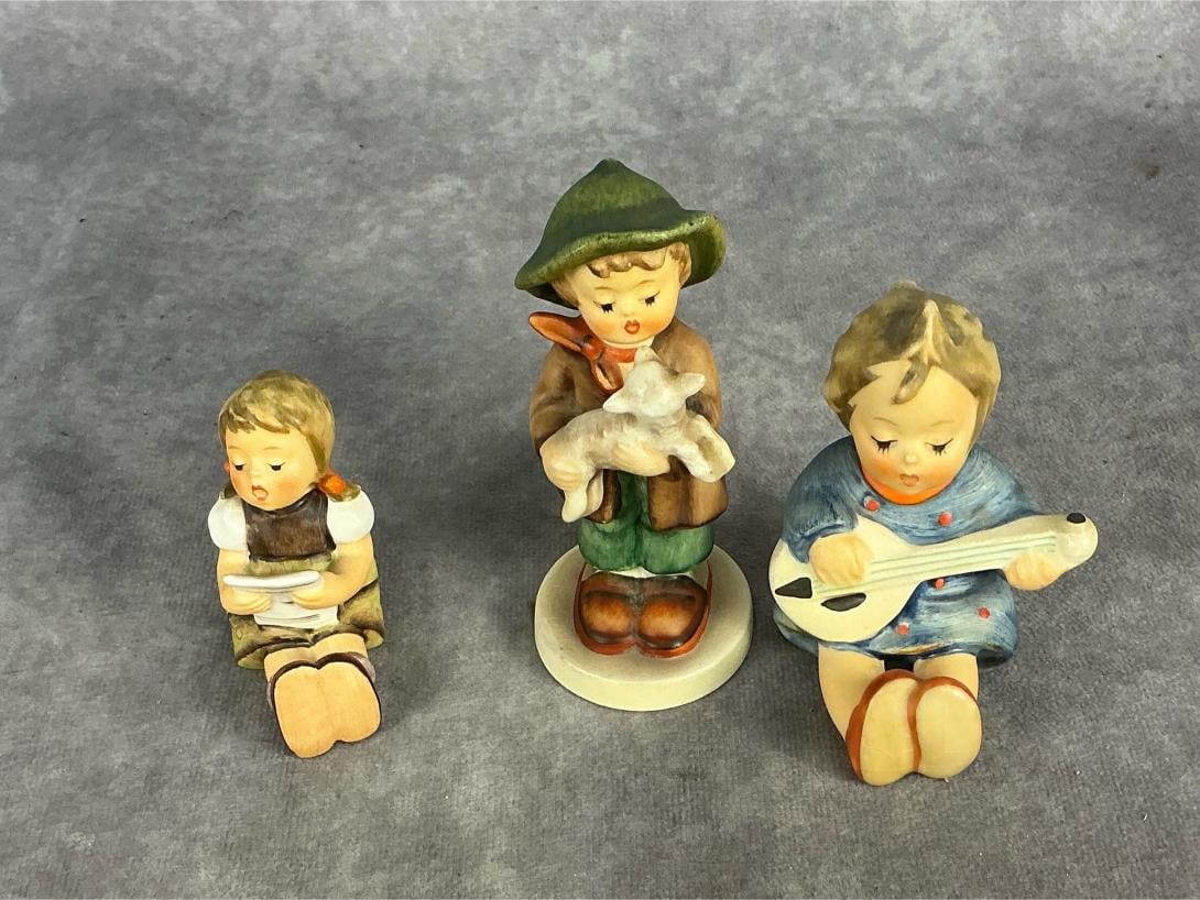 Vintage three mid 20th century German Hummel figurines. All marked W. Germany. Child reading book: Vintage three mid 20th century German Hummel figurines. All marked W. Germany. Child reading book marked "Goebel 385 85". Child holding lamb marked "Goebel 68/2/0". Child playing guitar possibly marke