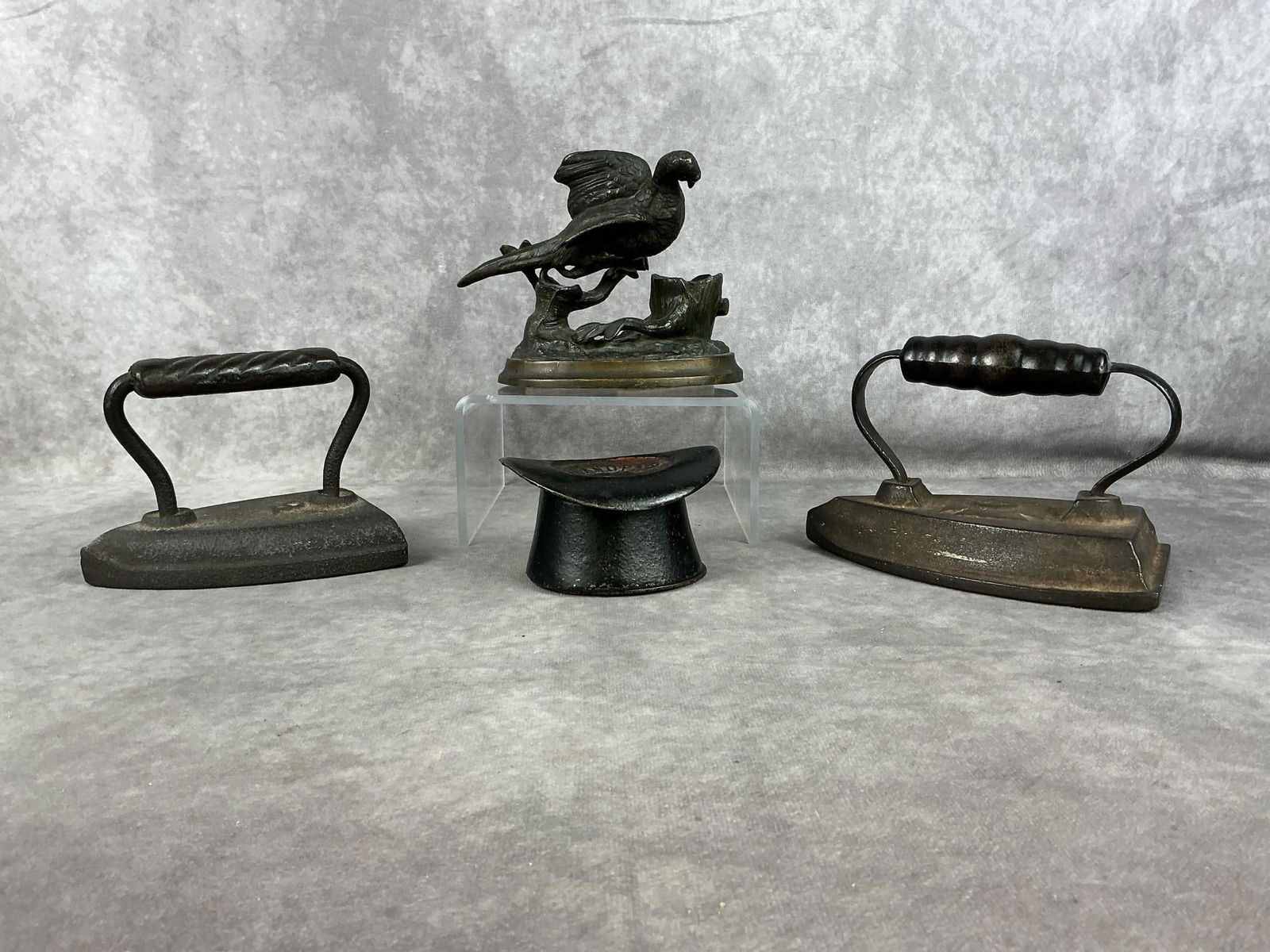 Cast Iron Collectibles: One Early 20th century cast iron "Grandpa's Hat" bank. Two late 1800's sad/flat irons marked "5" and the larger iron marked "6". One late 19th - early 20th century patinated bronze spelter sculpture o