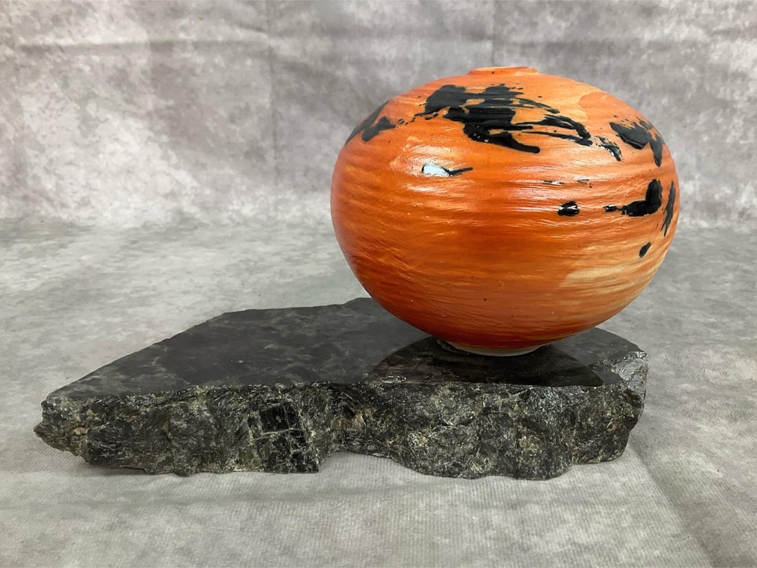 Otto Heino Art Pottery: Late 1900s pottery. Orange and black sphere vase by Otto Heino from Ojai, CA. Unique piece attached to polished stone base. Good condition. Art piece measures 8.5 inches long x 3.5 x 5 inches tall.