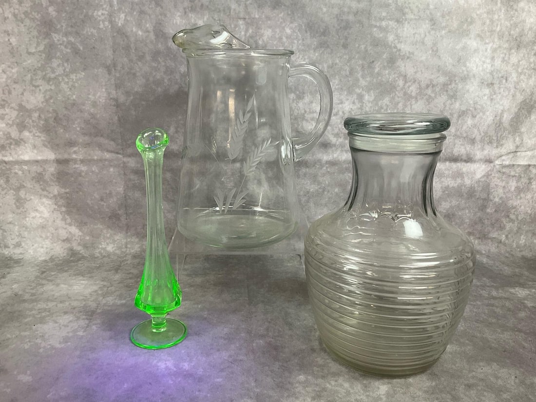 Vintage Pitchers & Uranium Glass Vase: Three mid century glass pieces. Uranium green Vaseline glass bud vase. Anchor Hocking glass beehive decanter with lid, and clear glass pitcher with etched wheat motif. In good condition. Beehive