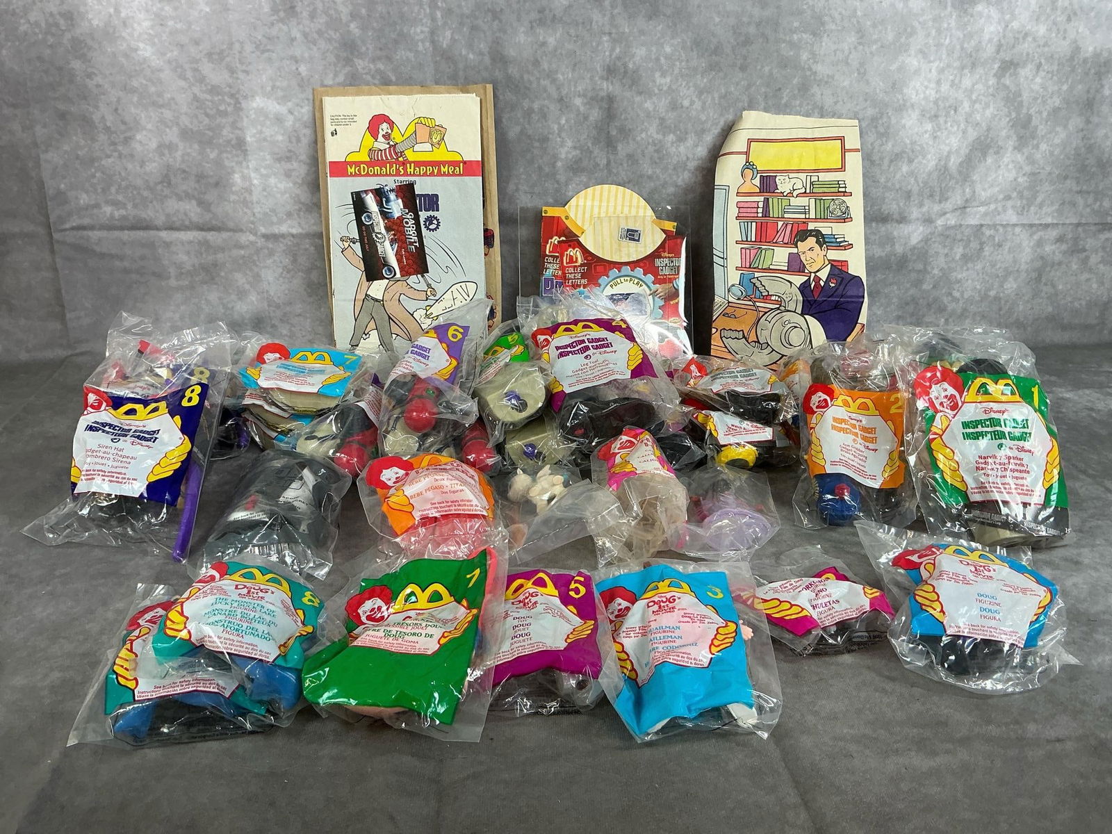 McDonald's Toys- Inspector Gadget & Doug's 1st Movie: Thirty-two 1996-1999 toys. 24 Inspector Gadget toys, 2 Hercules, and 6 Doug 1st Movie toys. In original packaging. Average package measures 5 inches wide x 7 inches tall.