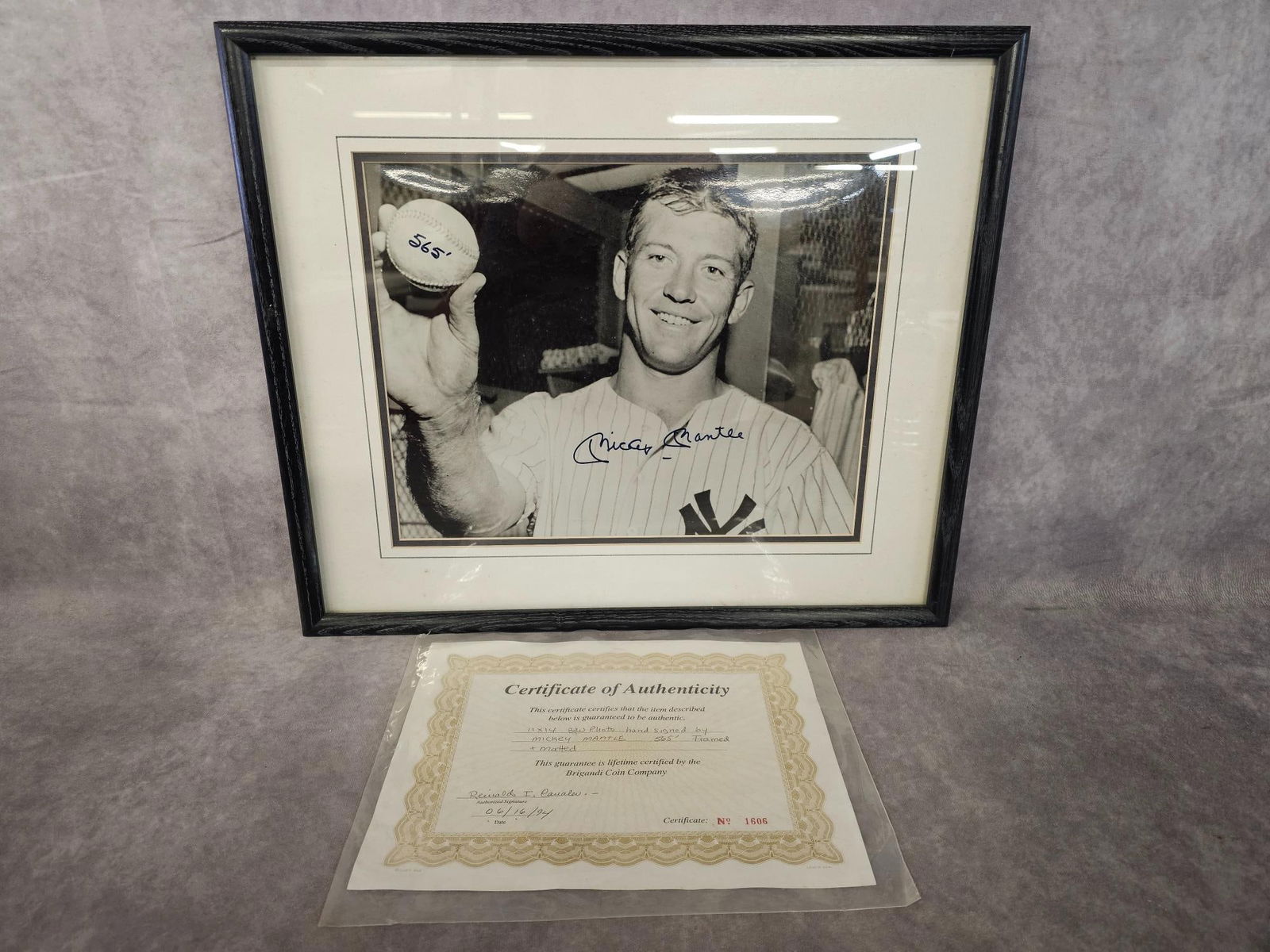 Signed Mickey Mantle Photo: Black and white framed photograph hand signed by Mickey Mantle comemmorating his 565 foot home run at Griffith Stadium in Washington D.C. COA from Brigandi Coin Company included. Measures 19.5 inches