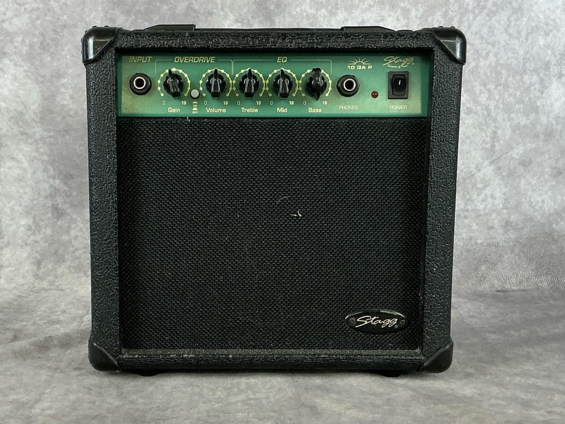 Stagg 10 GA P Amp: Model 10 GA P. No serial number found. Single input, gain and volume knobs, treble, mids, and bass equalizer, overdrive button. Used condition with wear and tear, amp housing unit loose. Tested, not