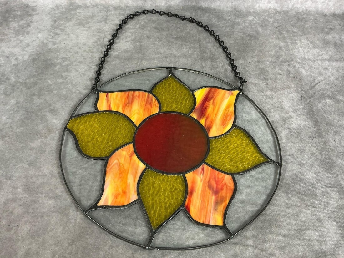 Stained Glass Flower: Hand crafted stain glass with flower in orange, green and yellow textured glass. With chain for hanging. In good condition. Measures 12 inches in diameter.