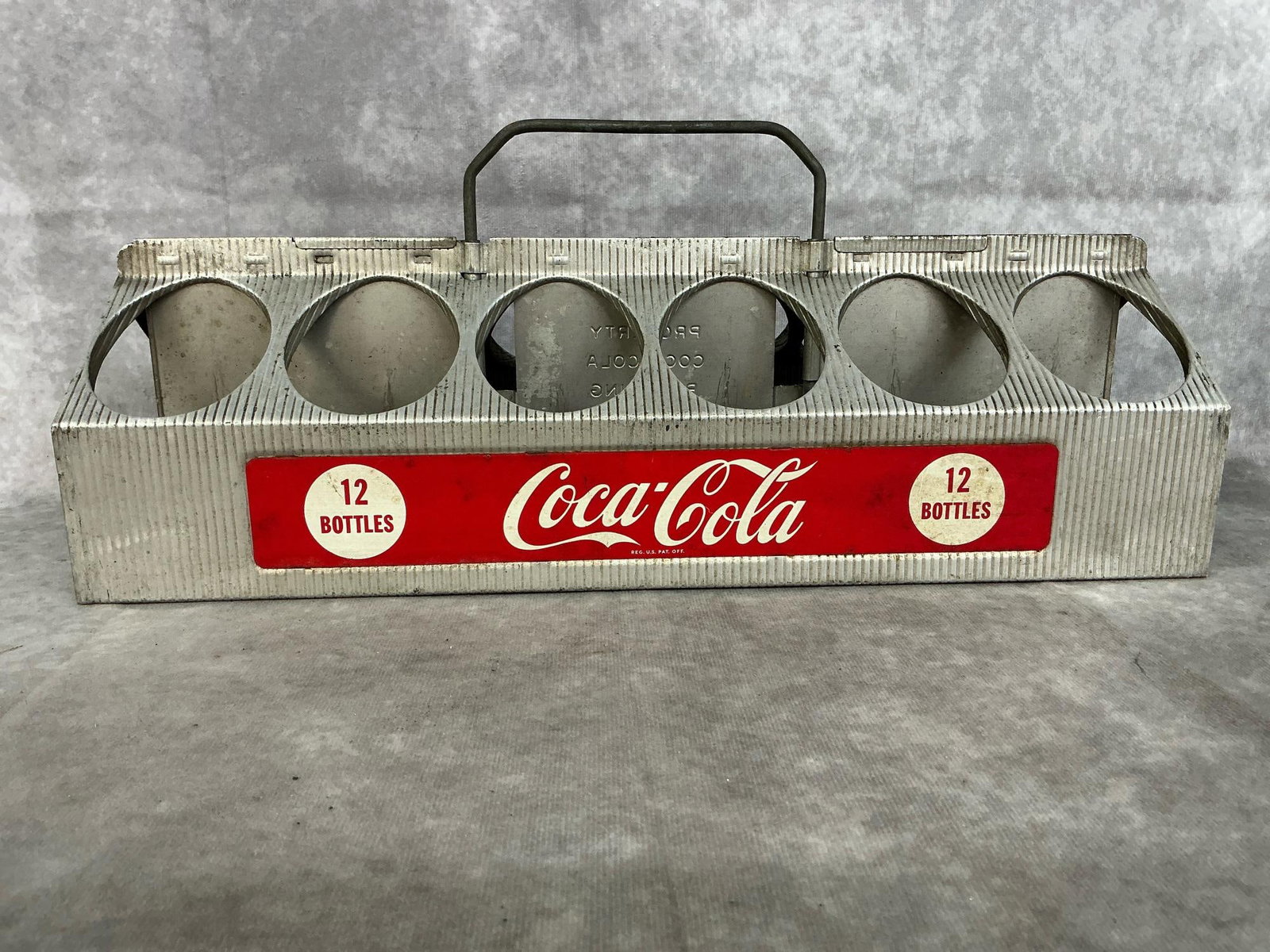 12 Bottle Coke Carrier: Mid century Coca-Cola carrier. Aluminum 12 bottle carrier with extendable handle. In good condition. Measures 16 inches long x 5.5 x 6.5 inches tall.