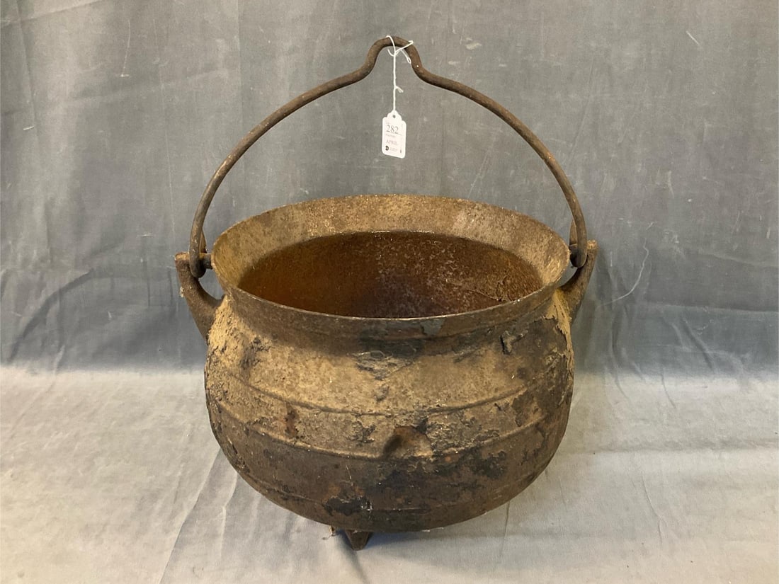 Early Iron Cauldron: Late 18th - early 19th century cast iron six gallon tripod foot cauldron with removable bail hanger/handle. Marked “6 G”. Signs of wear commensurate with age and use. No visible cracks or hole