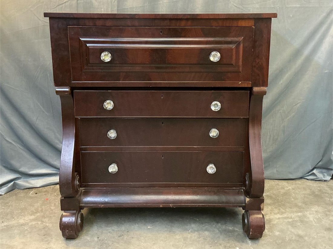 Mahogany Veneer Secretary Empire Desk: Scroll pilasters and original glass knobs. Secretary compartment over three drawers. One of the pillars is loose and there are scratches to the top and the front of the piece. Fair to good condition.