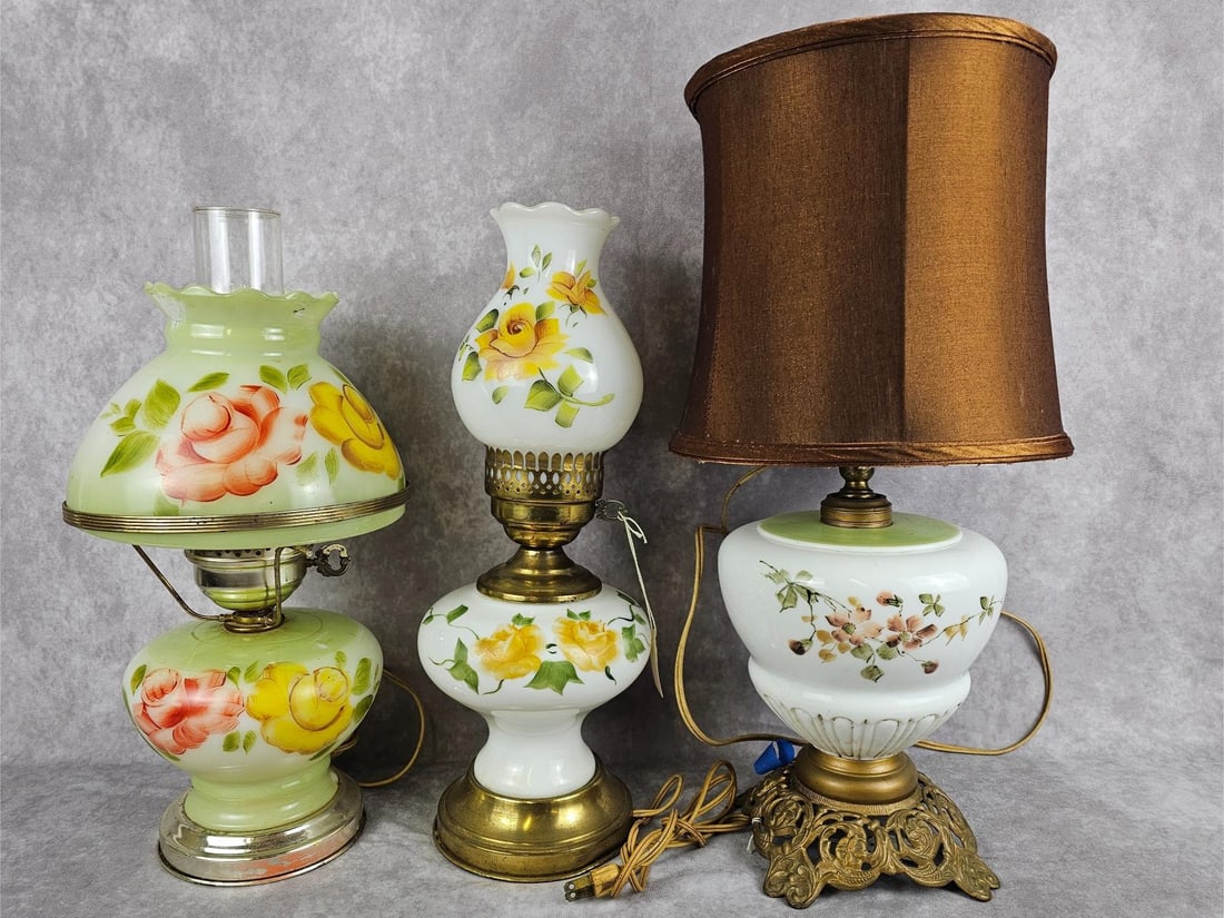 Hurricane Lamps: Three vintage hand painted hurricane lamps. All three tested and working. Tarnish to bases, green lamp has a chip at base, some wear to paint, finial missing on fabric shade. Largest measures 7.5 inch