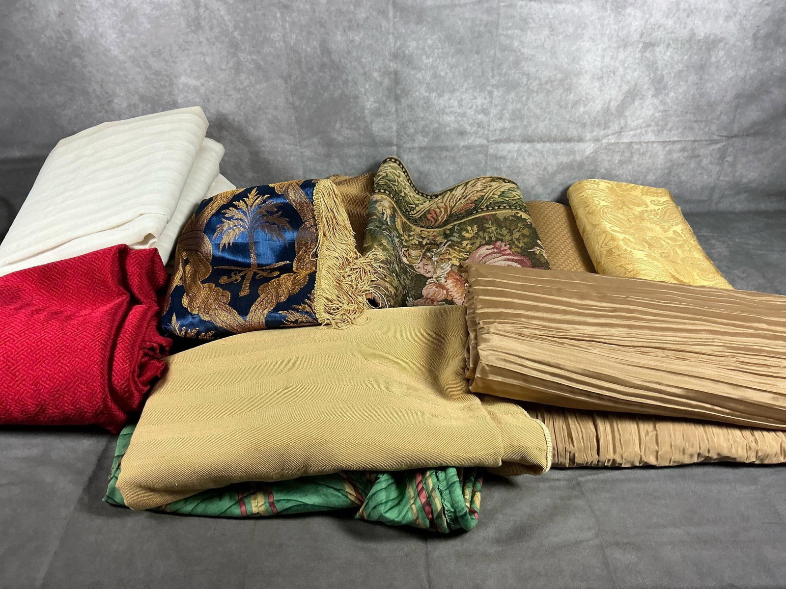 Tablecloths, Tapestry, & Drapes: Thirteen modern household fabrics. Three off white drapes, a tapestry, and eight tablecloths in varied colors, fabrics, and patterns. A few stains, otherwise in good condition.