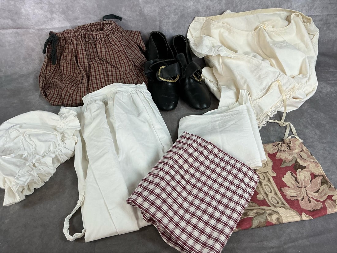Women's Reenactor Clothes: Eight pieces of 1700s reenactor's clothing. Includes plaid skirt with drawstring, long white apron, white nightgown with drawstring neck, neckerchief, bonnet, and cloth sack. Black ladies shoes with g