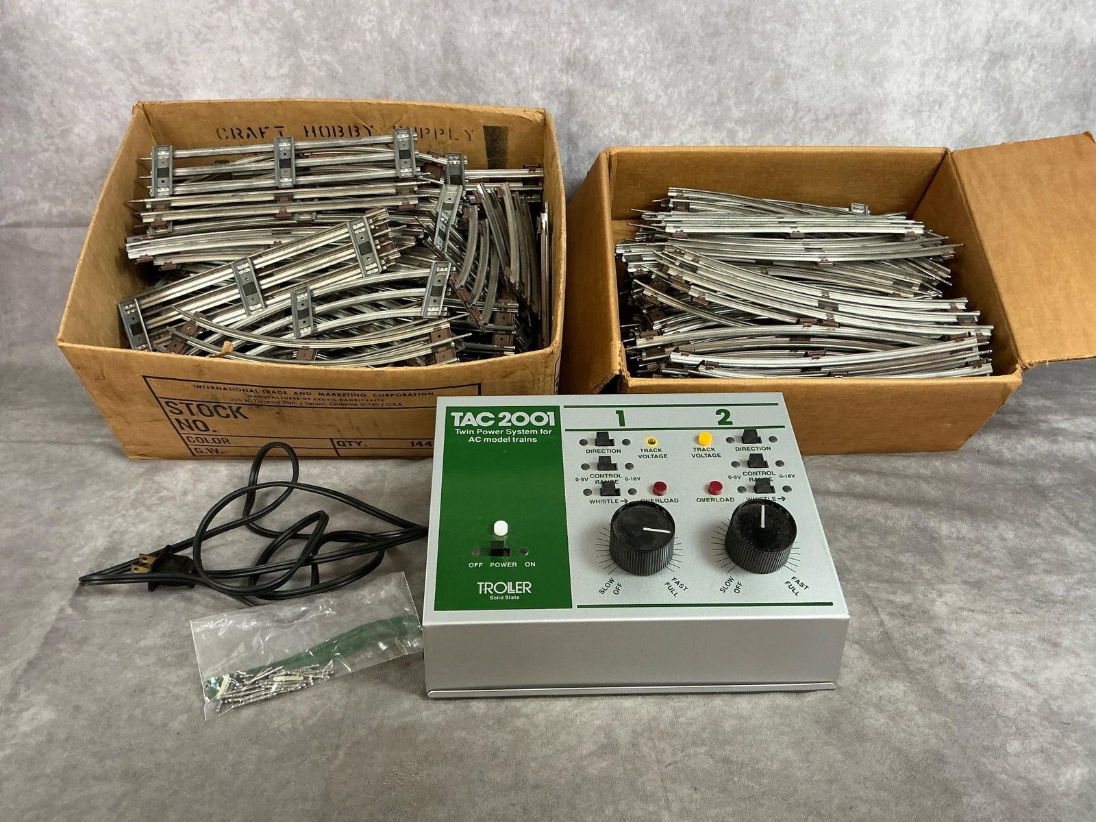 Model Train Power System & Tracks: Vintage power system and train tracks. Troller TAC2001 twin power system for AC trains and two boxes of 027 gauge tracks. Troller box powers on, otherwise untested. Tracks are used but appear to be