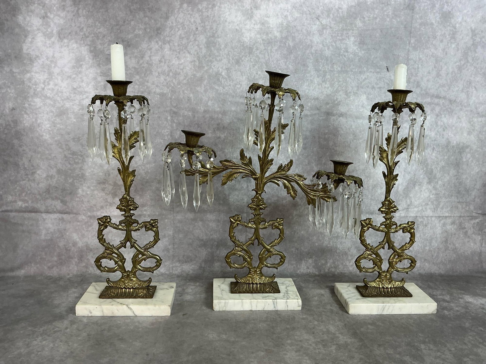 Girandole Candelabras: Three early 1900's brass and marble candelabras. Rococo style with hanging crystal prisms on marble base. Three candle holder leans slightly to one side, otherwise in good condition. Largest measures 