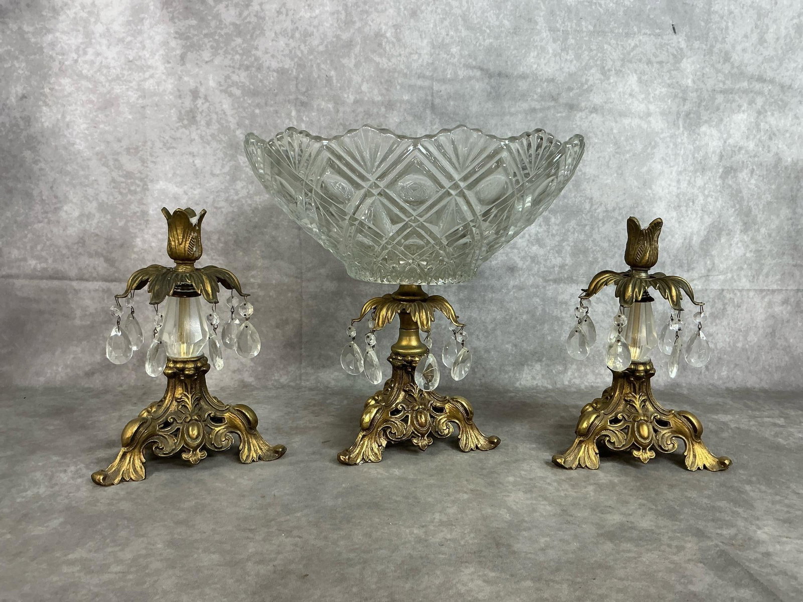 Baroque Style Centerpiece Bowl & Matching Candle Holders: Three vintage cut glass and brass-toned metal pieces. Compote fruit bowl centerpiece with scalloped rim. Pair of matching candle holders with hanging crystal prisms. In good condition. Bowl measures