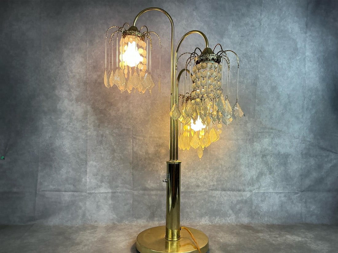 3-Light Chandelier Style Lamp: Vintage table lamp has three arched arms with crystal accents and gold tone base. One socket untested due to broken bulb. Some scratches on base. Measures 10 inches in diameter at base x 34 inches