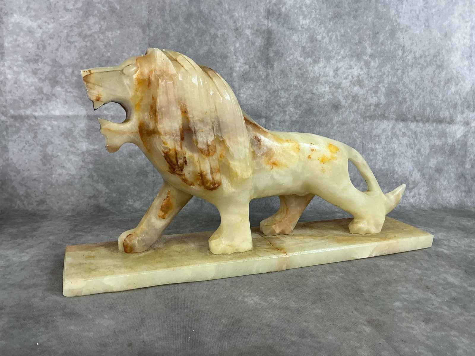 Marble Lion Sculpture: Vintage hand carved marble lion. Gold and brown swirls in onyx stone. Center of base is broken. Measures 16 inches long x 3.5 x 8.5 inches tall.