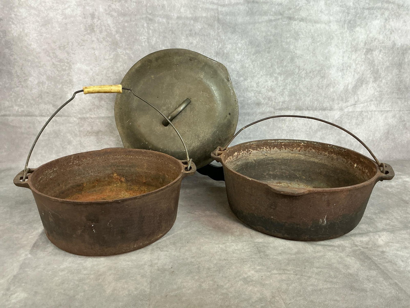 Cast Iron Pots: Two vintage cast iron pots and a lid. Largest pot is 11.5 inches in diameter x 4 inches tall, smaller measures 10.25 inches in diameter x 4 inches tall. Lid is 11.5 inches. Rust and discoloration