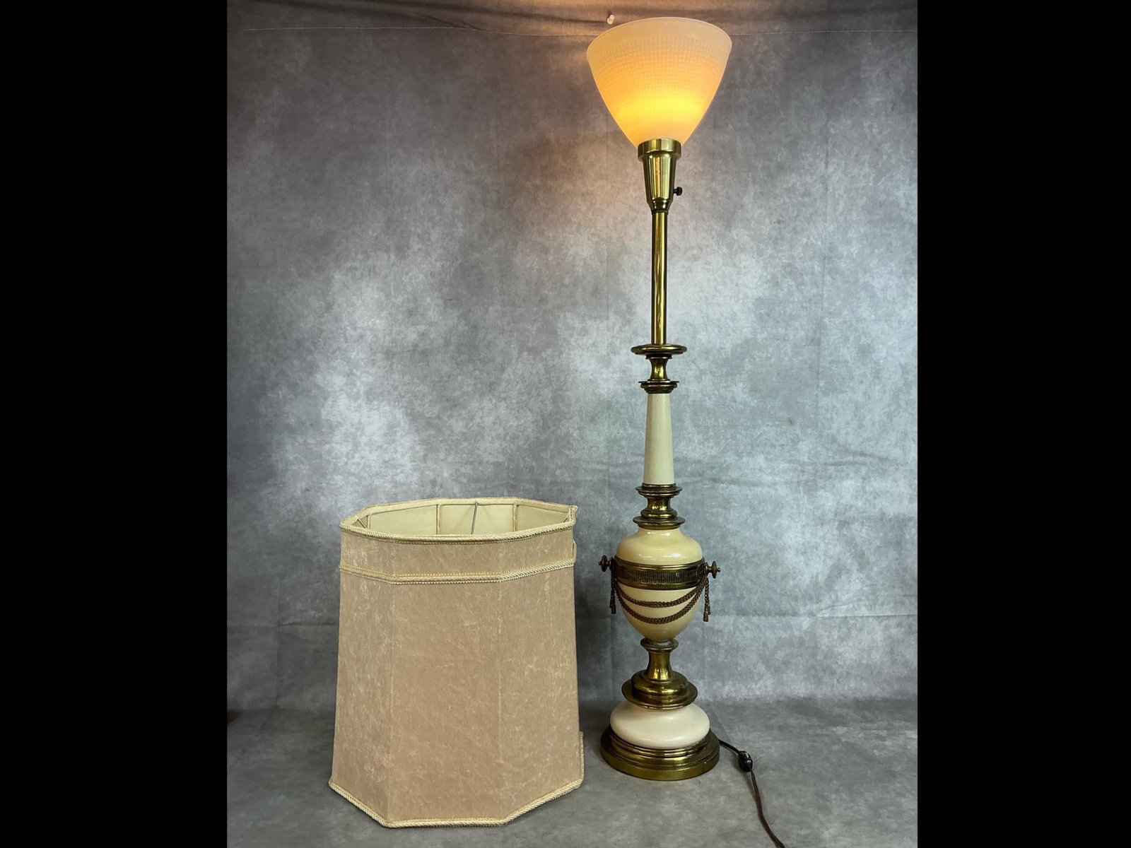 Hollywood Regency Table Lamp & Shade: 1960's table lamp and hexagonal shade. Hollywood regency style with brass and porcelain urn body. Separate cream colored velvet feel lamp shade. Slight color fade and tarnish on lamp, otherwise in