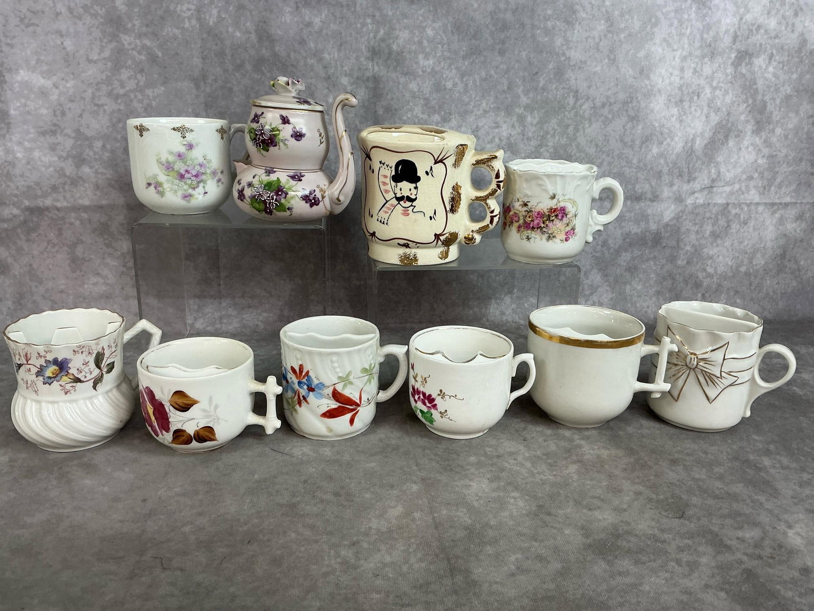 Vintage Mustache Cups & Violet Teapot Set: Ten mid 1900's cups. Nine mustache cups in varied designs and Victorian Violets mini tea set by Lefton's Exclusives. Slight paint loss at rims, and some crazing. Otherwise in good condition. Largest