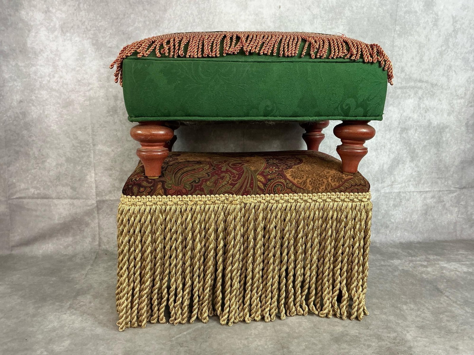 Victorian Footstools: Two vintage decorative footstools with fringe. Brown and burgundy paisley print with long bullion fringe. Green fabric stool with floral needle point top. Both have wooden legs. Slight wear,