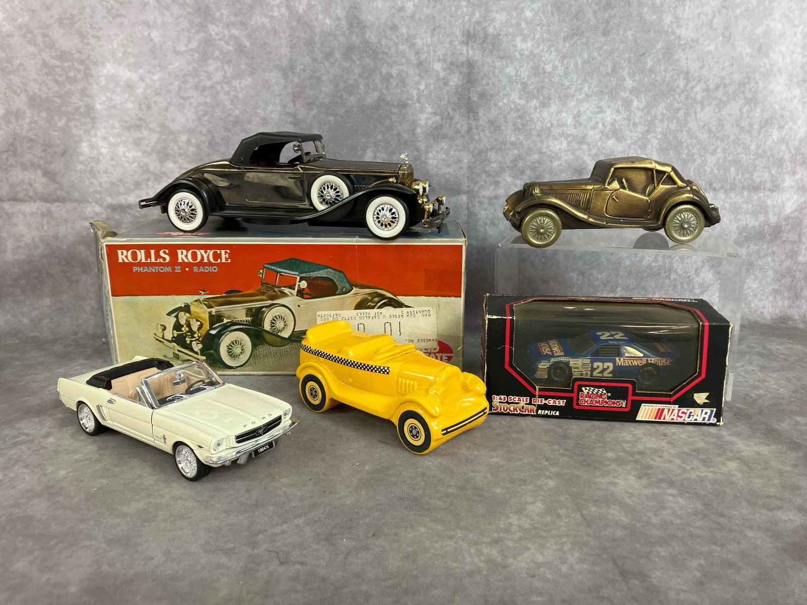 Collectible Cars: Five cars from early to late 1900's. Includes Rolls Royce Phantom II Radio, Gate City savings bank antique car, Avon Taxi bottle, Die-Cast NASCAR #22, and white metal Mustang replica. Boxes are worn,