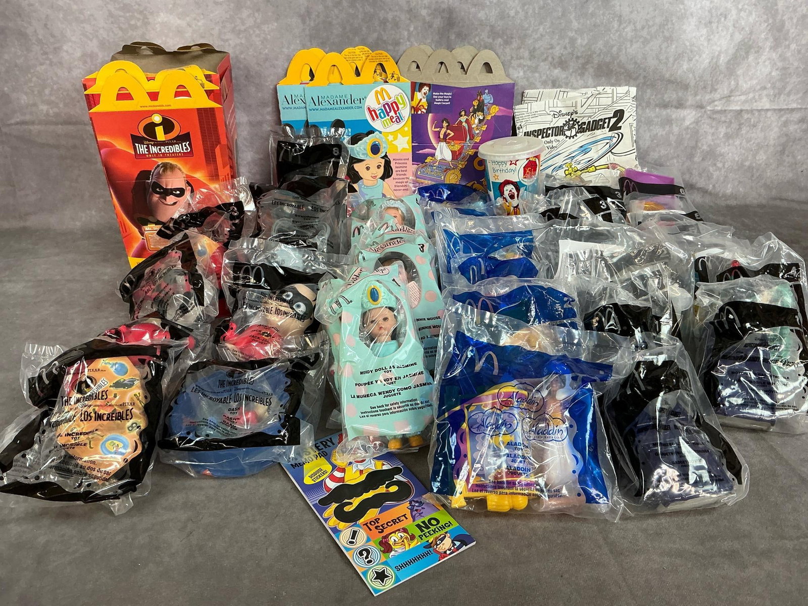 McDonald's Meal Toys: Thirty-nine Happy Meal toys from 2002-2004. Including The Incredibles, Madame Alexander Dolls, Disney's Aladdin, and Inspector Gadget. All in original packaging. Average size is 4 inches wide x 5