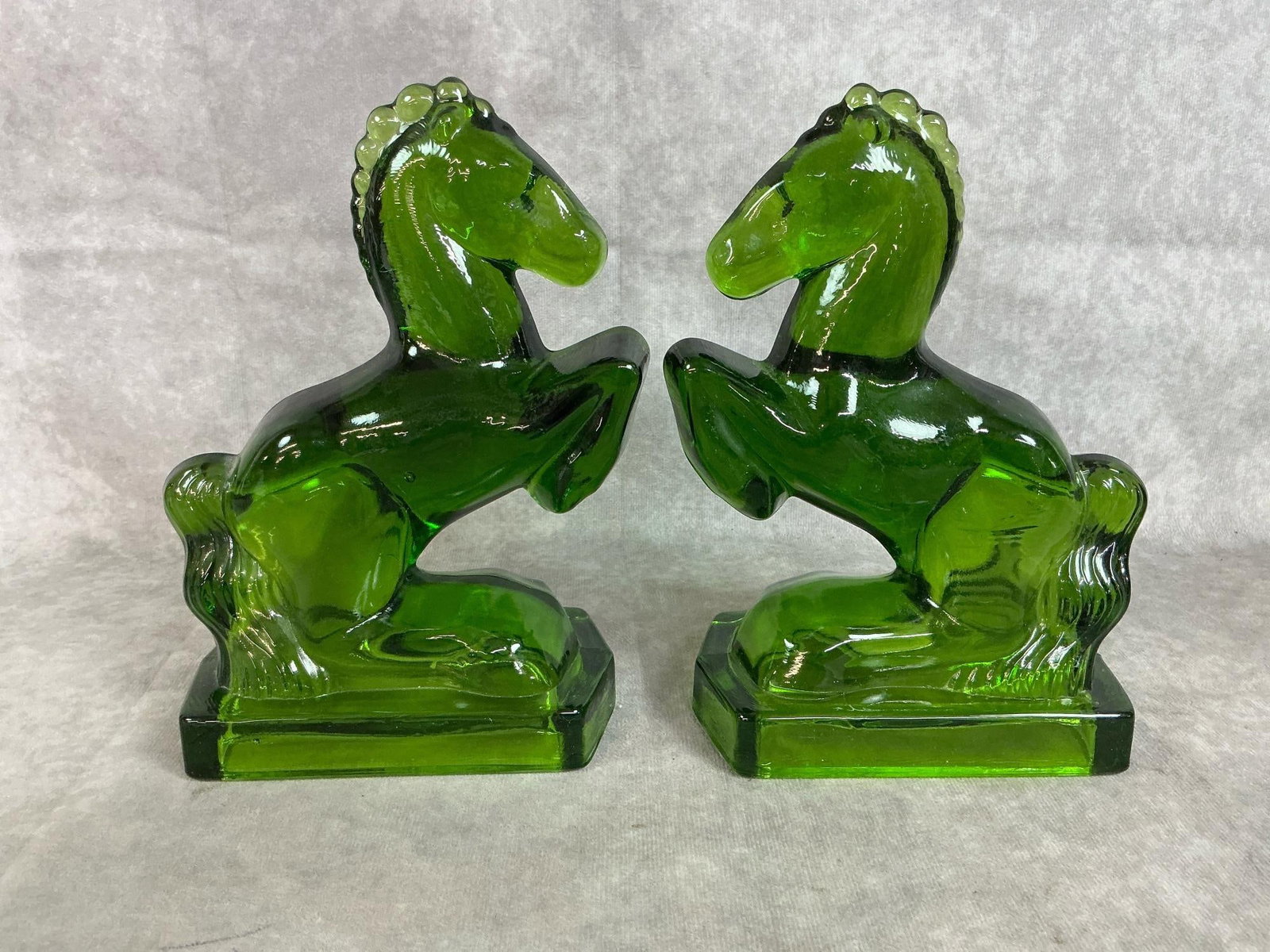 L E Smith Green Glass Horses: Two 1950's emerald green horses. Handcrafted by Smith heavy glass horse bookends. In good condition. Each measures 5.25 inches wide at base x 3 x 8 inches tall.