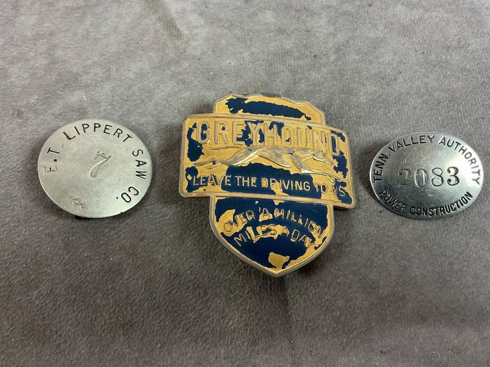Employee Badges: Three vintage employee badges. Greyhound driver's badge, E T Lippert Saw Company, Pittsburgh, PA, 1920's badge, and Tenn Valley Authority badge. Greyhound badge has paint loss, otherwise all in good