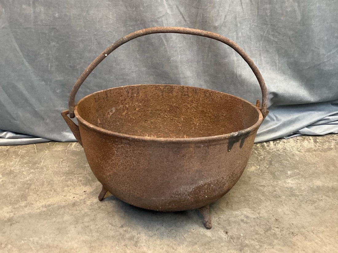 Cast Iron Cauldron: Early 19th century cast iron cauldron with tripod legs and detachable bail handle. Some loss to one leg and rust, otherwise good condition. Measures 22 inches in diameter x 12.5 inches tall.