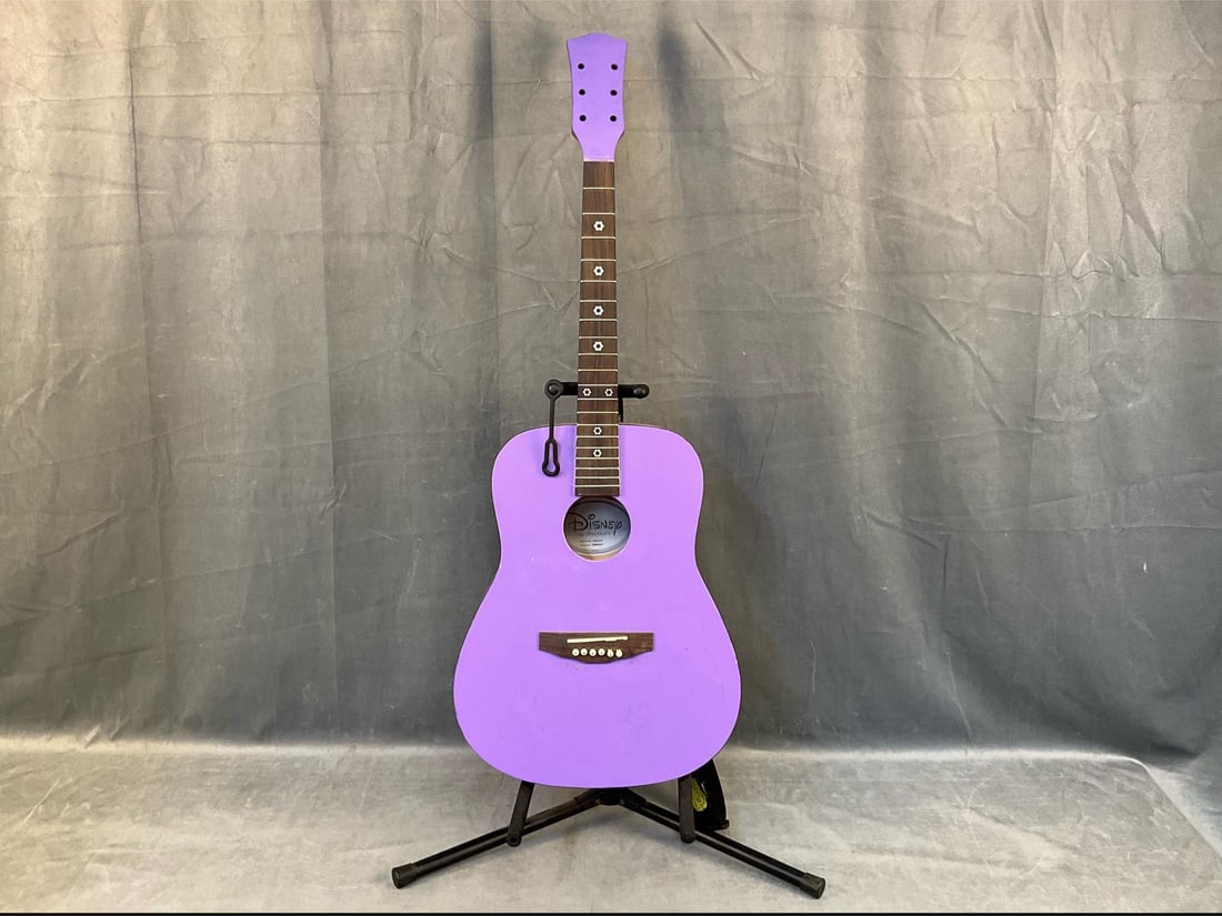 Washburn Acoustic Guitar: Late twentieth century vintage Washburn acoustic purple guitar by Disney with stand, has been painted purple. Model number HMDA 34. Missing tuning pegs, nut, and repainted facade. Measures 14 inches