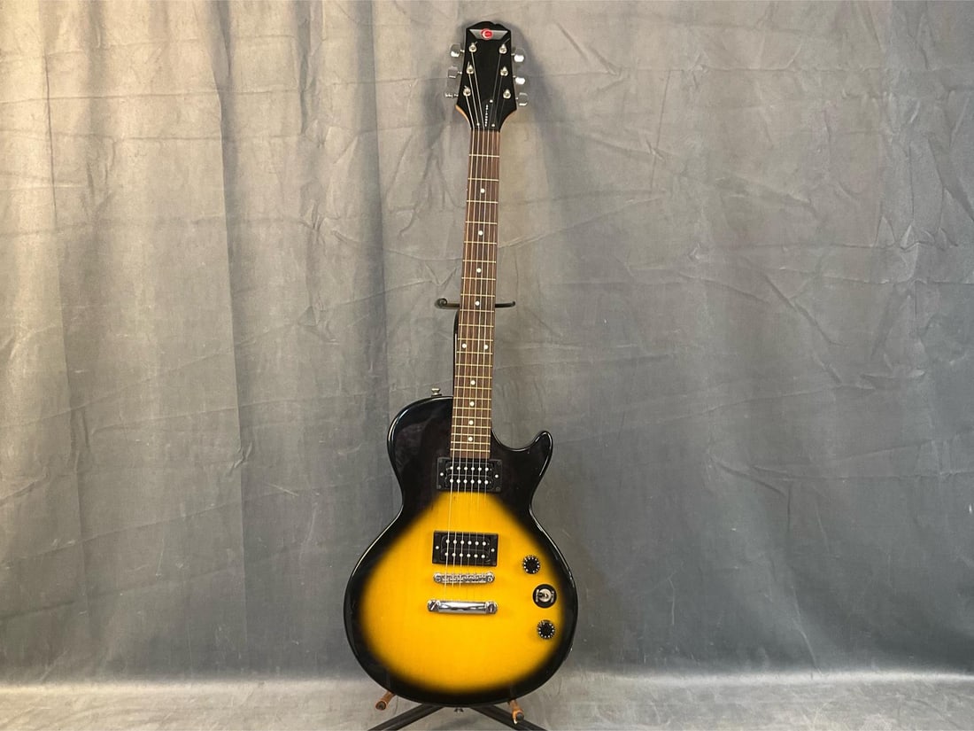 Epiphone Electric Guitar: Late 20th century Epiphone vintage electric guitar with soft case. Serial number- G01020852. Tested, powers on. Good condition. Measures 39.75 inches wide x 2 x 13.5 inches tall.